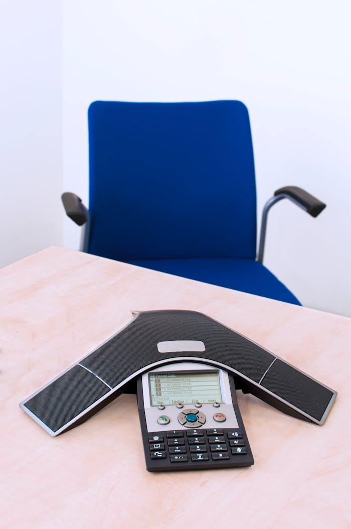 services-02 An office desk setup featuring a modern conference phone and a blue chair.