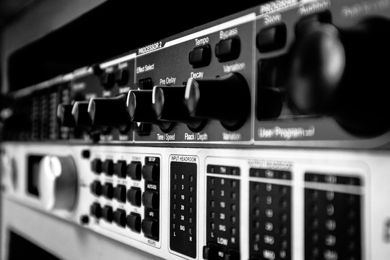 about-02 Detailed black and white close-up of an audio mixer highlighting various control knobs and switches.