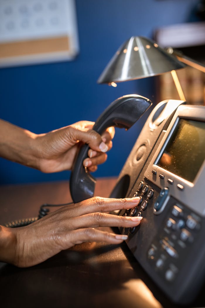 services-03 A person dialing a phone call on a desk telephone, focusing on hand details.