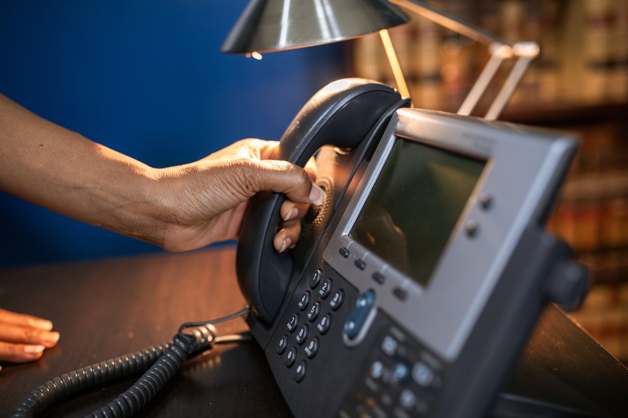 services-01 A close-up image of a hand picking up a handset from an office telephone, emphasizing communication device usage.