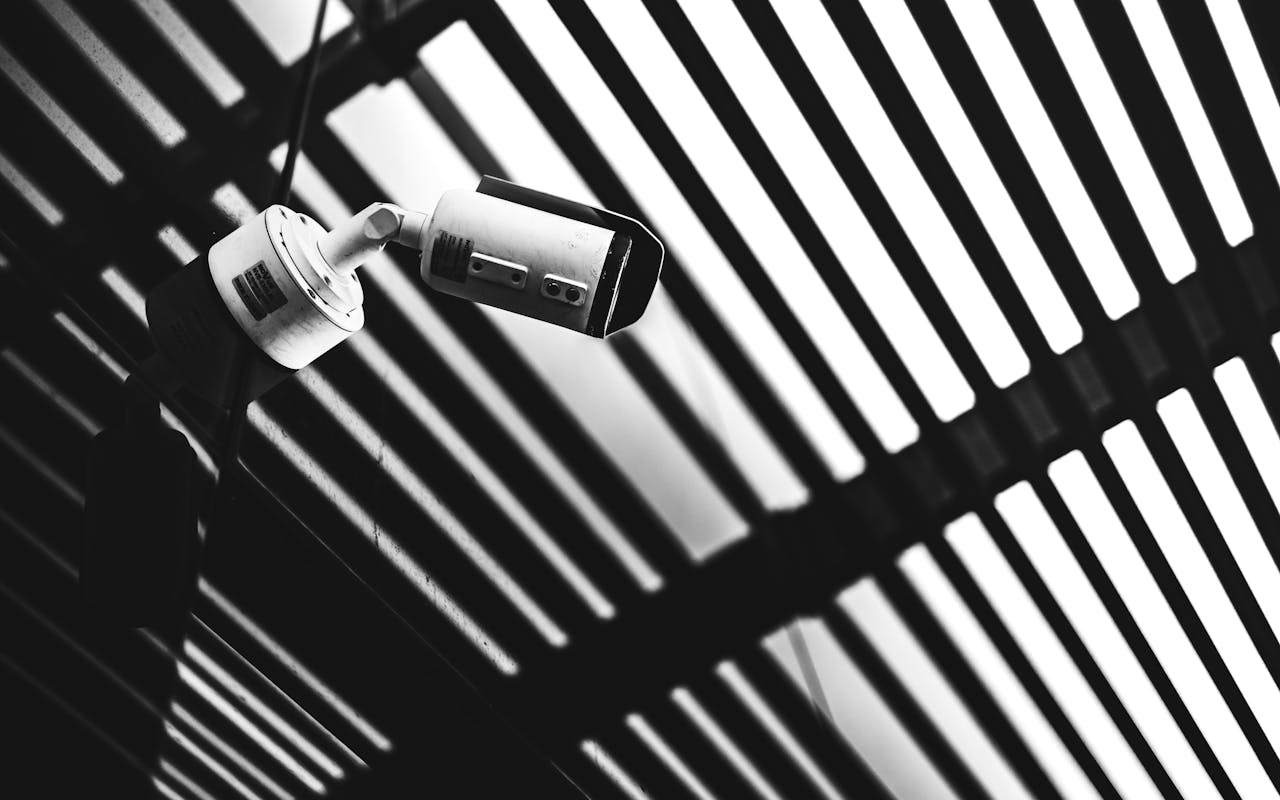 ours-journey Black and white CCTV camera capturing geometric shadows under a modern structure.